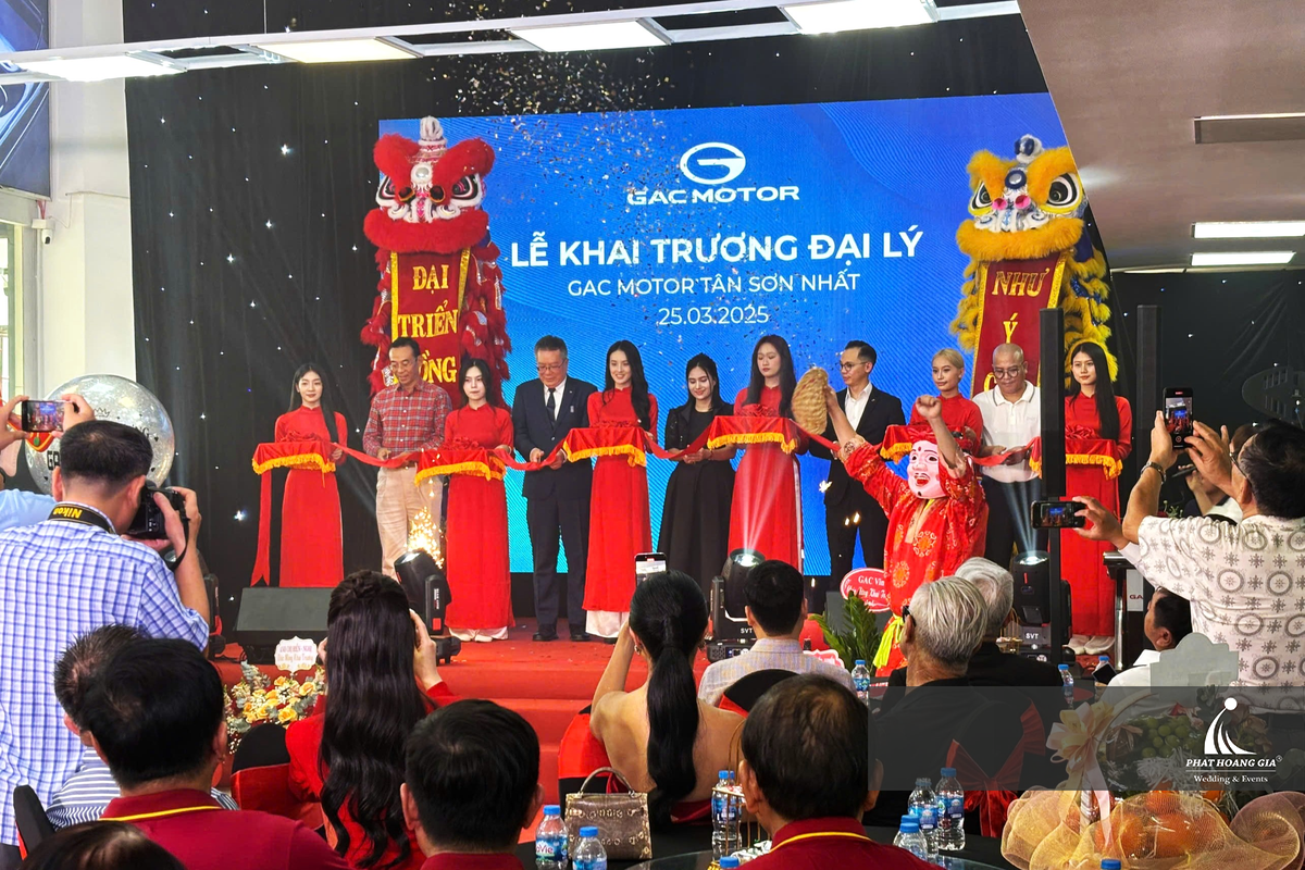 Nghi thức cắt băng khai trương với màn hình LED hiển thị nhận diện thương hiệu và thông tin sự kiện phía sau sân khấu